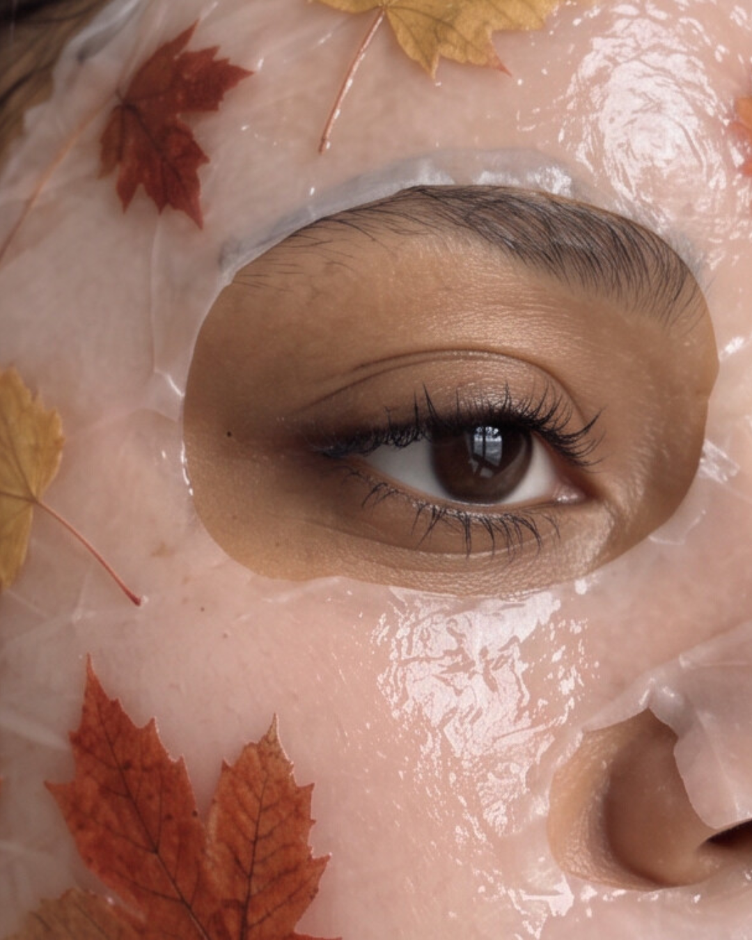 Close-up of a hydrating sheet mask on glowing skin, decorated with autumn maple leaves