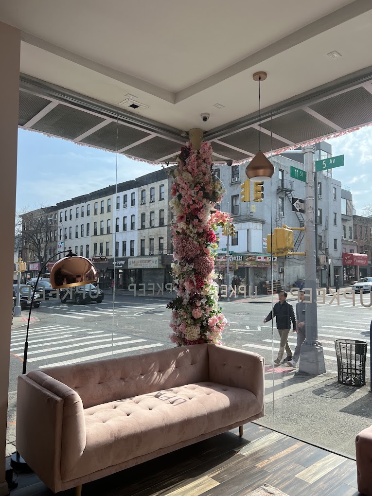 Inside UPKEEP Med Spa Brooklyn: a pink sofa and floral column at the corner window overlooking 5th Avenue and 11th Street in Park Slope